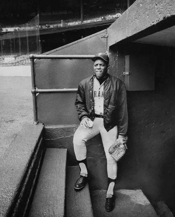 Willie Mays mặc áo khoác và đồng phục cầm quả bóng chày đứng trong khu vực kỹ thuật